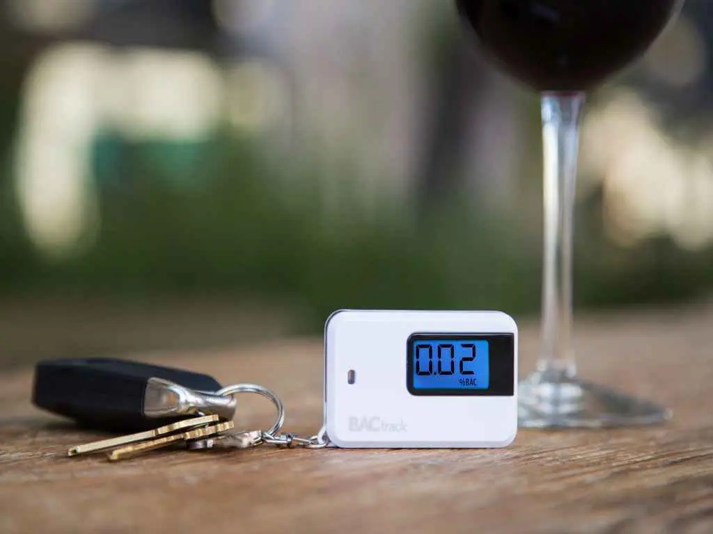 A keychain breathalyzer on a table with a glass of alcohol