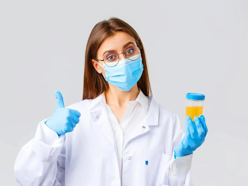 A woman holding a urine sample on her left hand while showing an okay gesture using her right hand