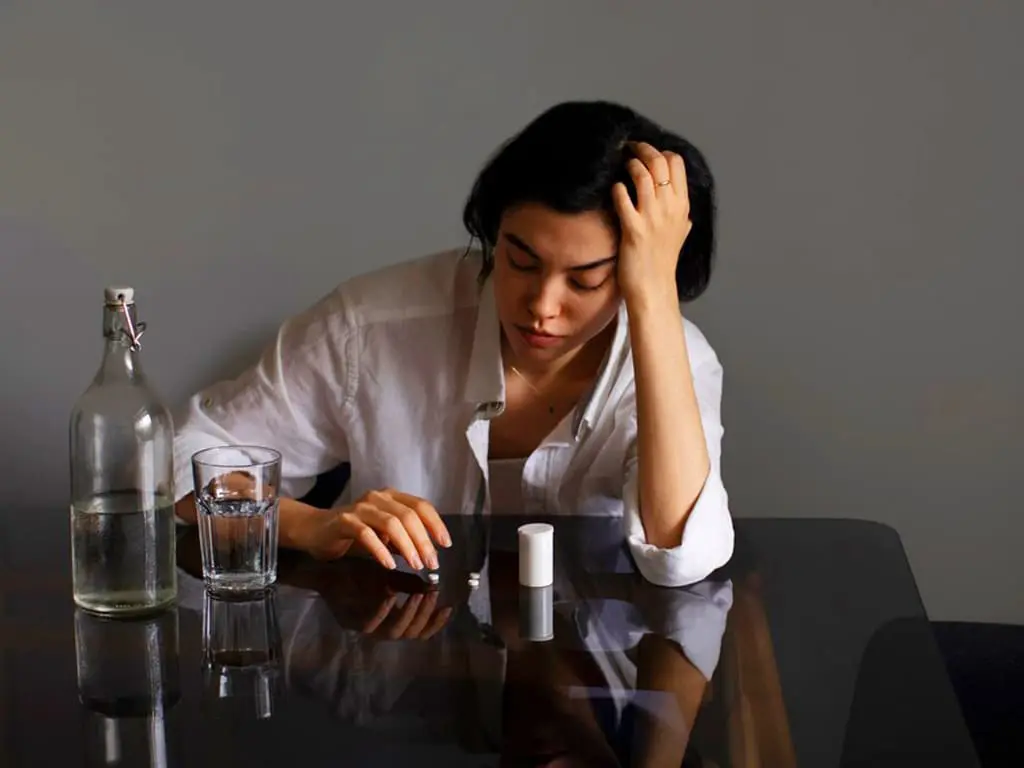 A woman taking pills with alcohol next to her