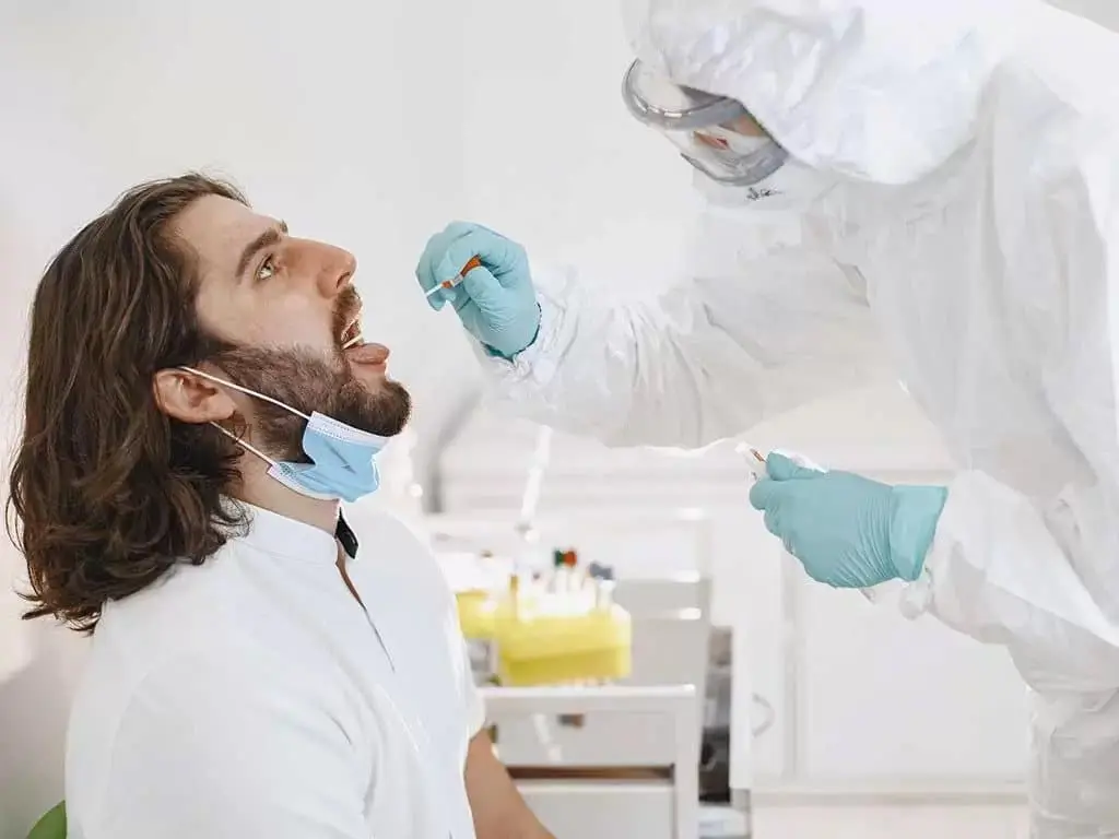 A lab technician wearing PPE swabbing a man