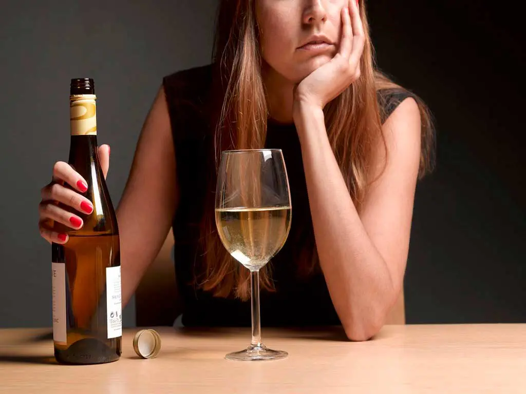 A woman holding a bottle of alcohol while a drinking glass is in front of her