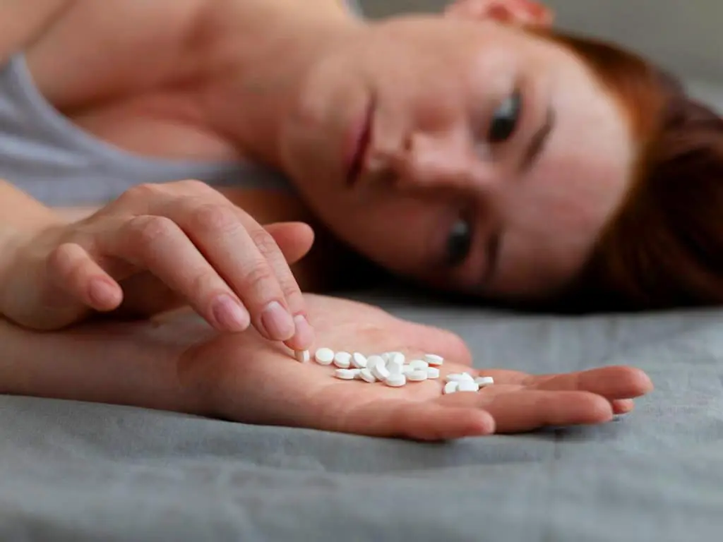 A woman lying down and looking at the white tablets in her hand