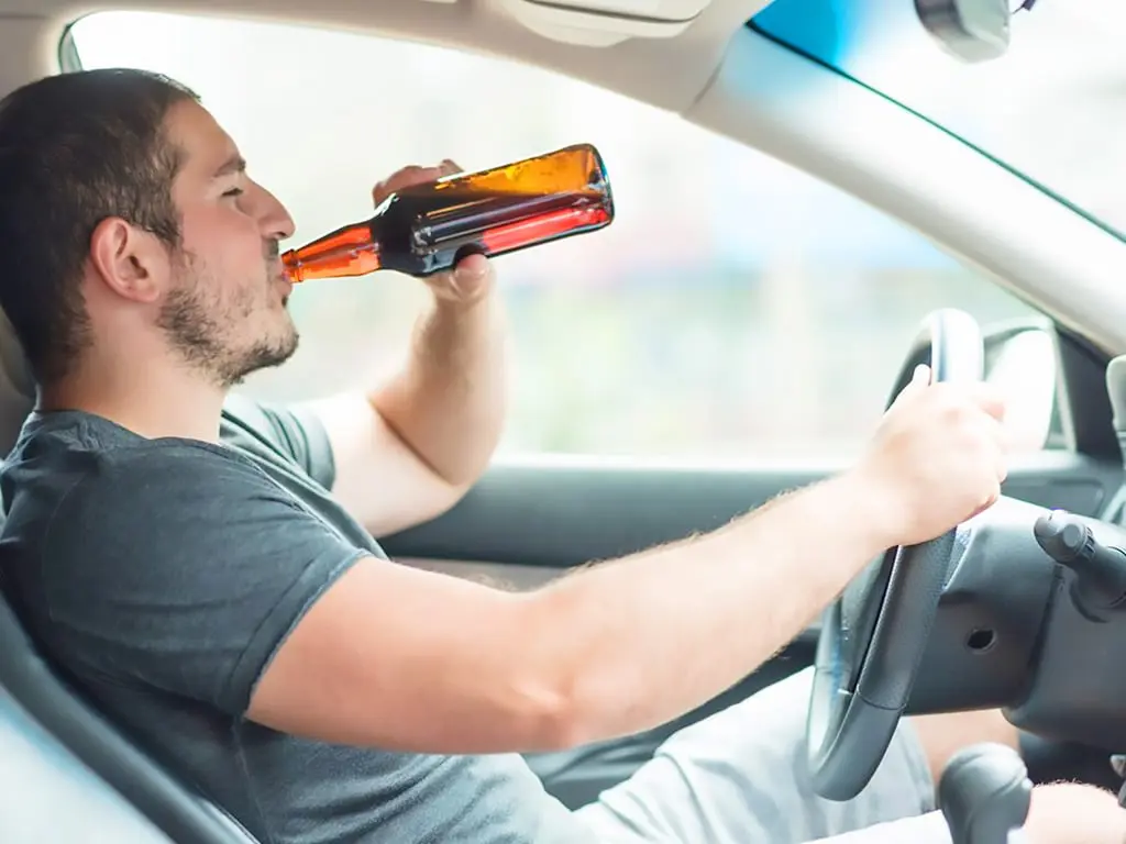 A male individual drinking beer while driving
