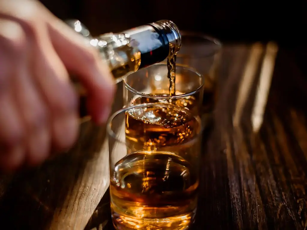 A person filling a glass with an alcoholic drink