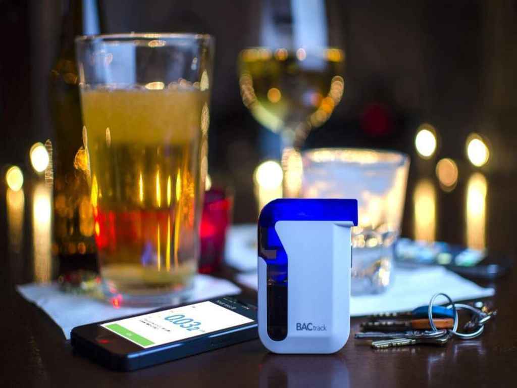 Glasses of alcohol, a phone, keys, and a breathalyser on a table