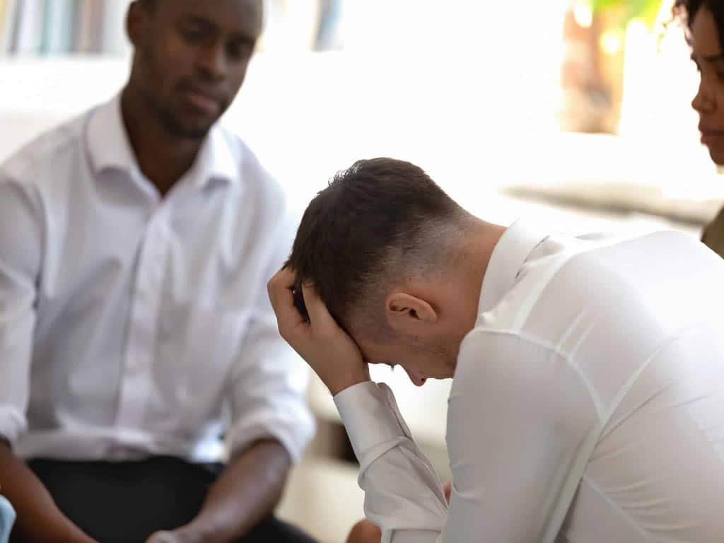 A man looking distressed while two other people are watching him