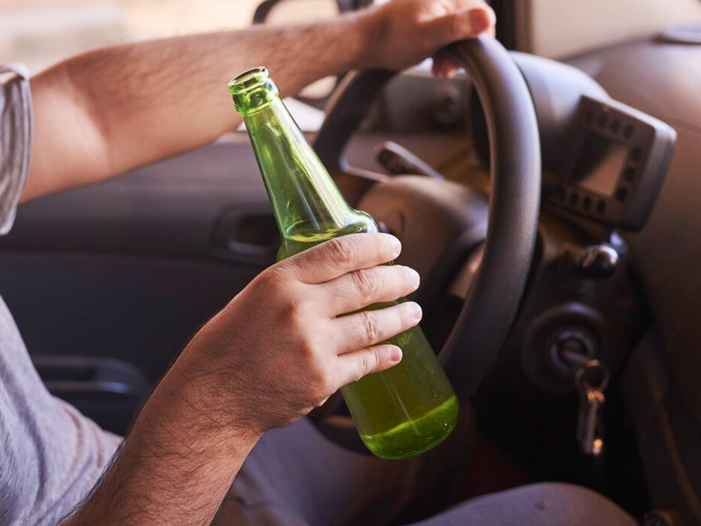 A man holding a beer bottle while driving