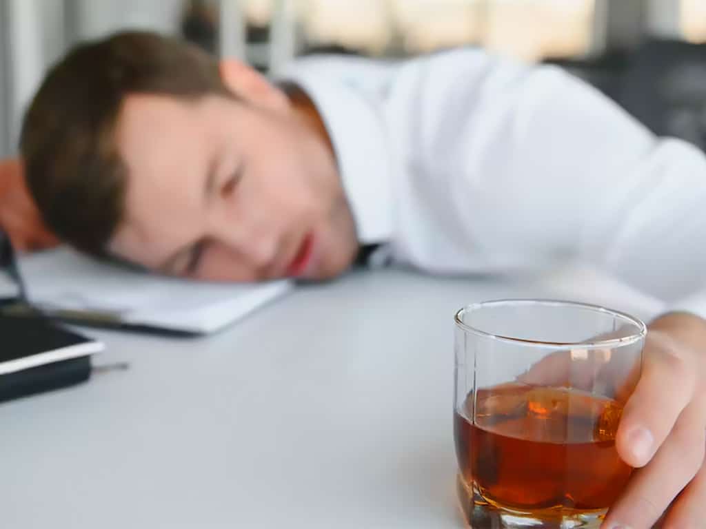 A man passed out on his table holding a glass of alcohol
