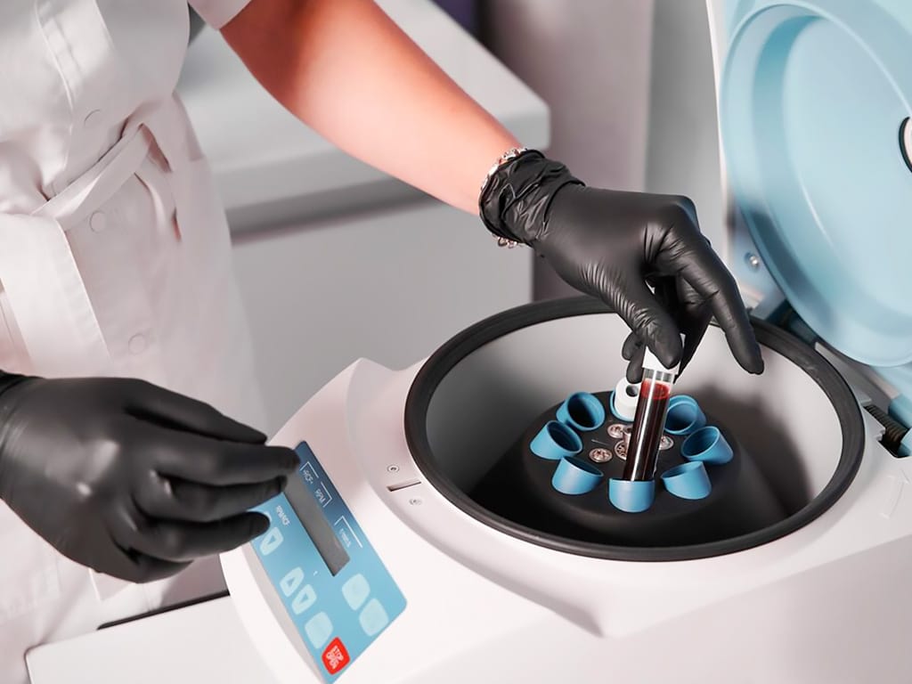 A lab professional placing a blood vial into the centrifuge