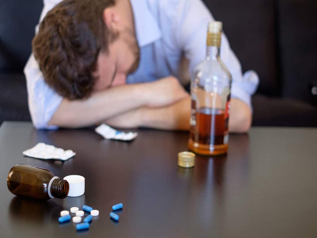A man sleeping while there are drugs and a bottle of alcohol on the table
