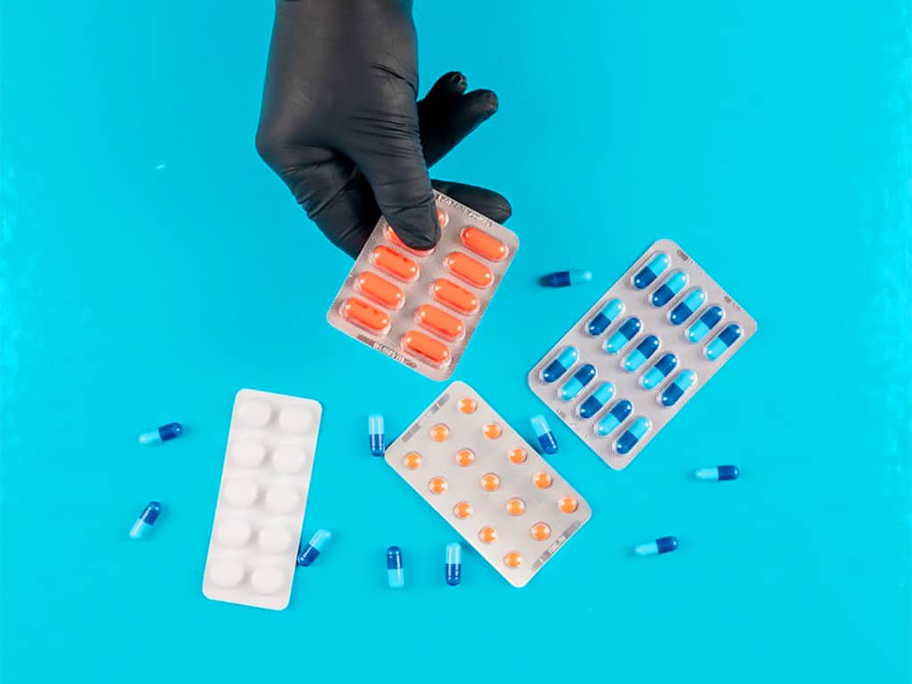 A person holding a pack of drugs with other pills surrounding them