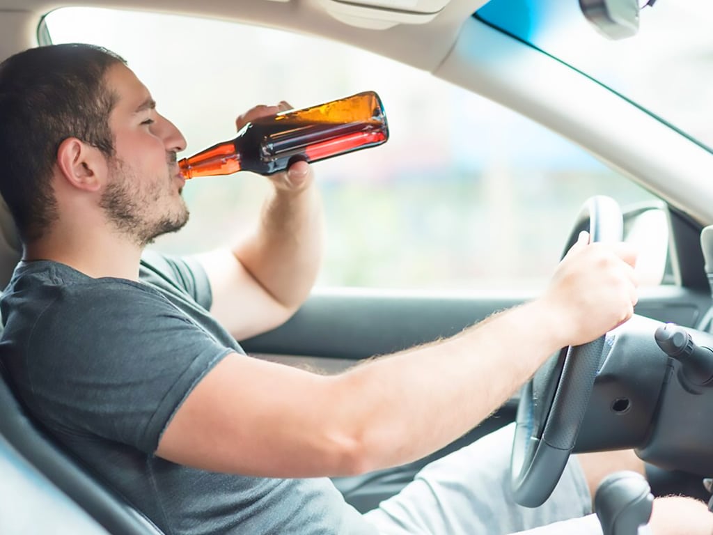 A man drinking beer while driving a car