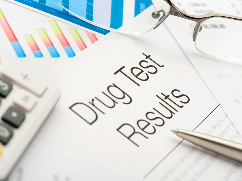 A drug test result document covered with a pair of glass, calculator, and pen