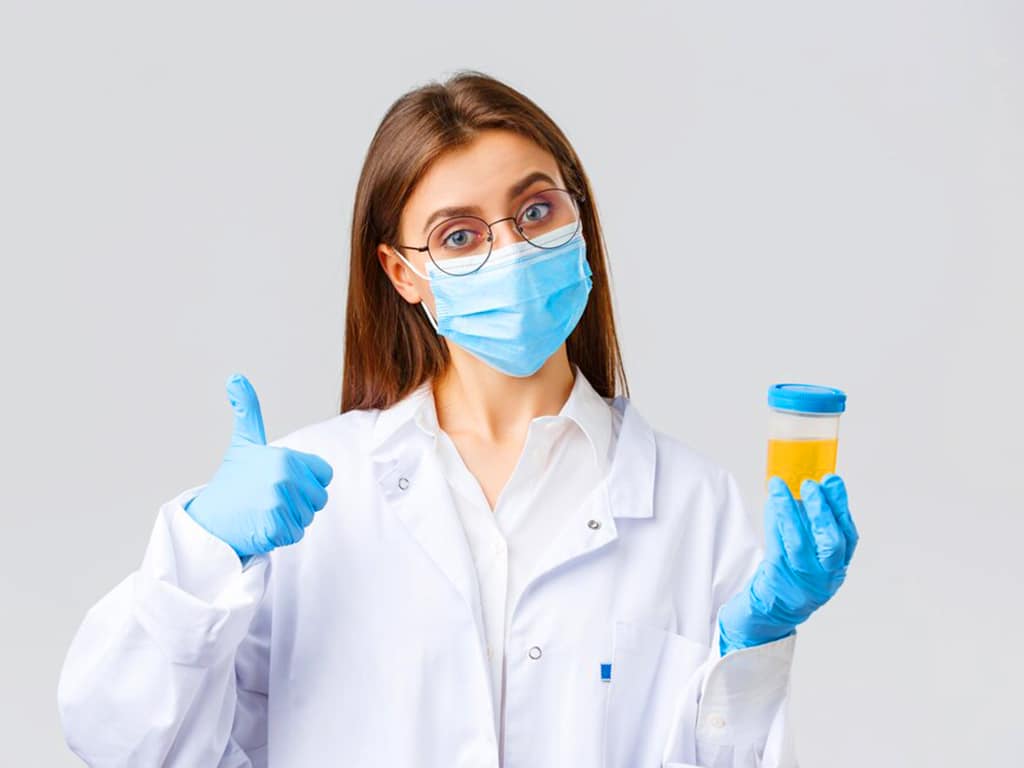 A lab professional holding a urine sample in a cup